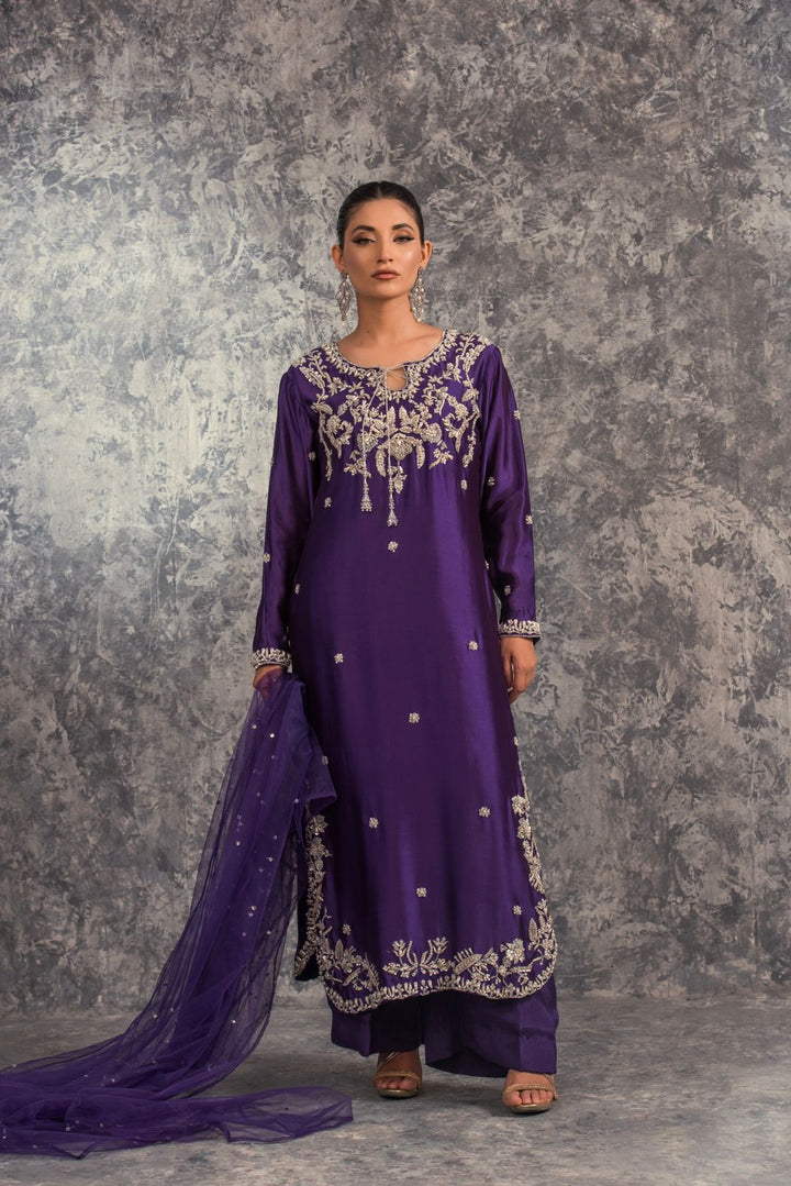 Woman wearing a purple embroidered traditional outfit against a textured gray background