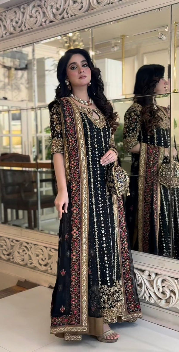 Woman in a black and gold embroidered dress standing in front Haris Shakeel - zainab pakistani indian wedding bridal dress, mehndi nikkah oufits guest suitsof a mirror.